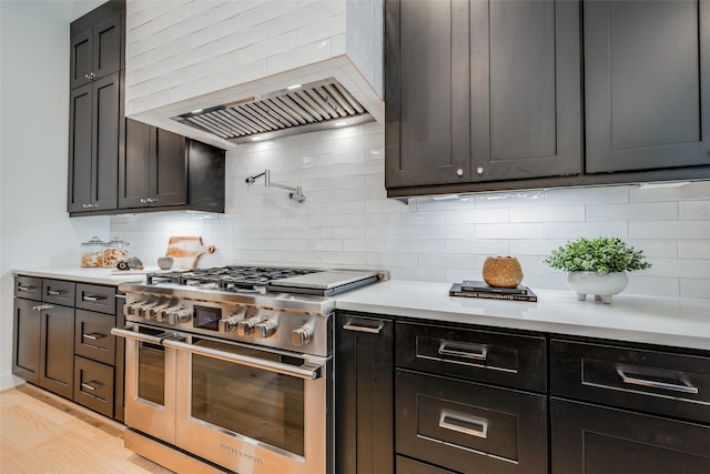 kitchen with double oven range, premium range hood, backsplash, and light hardwood / wood-style flooring