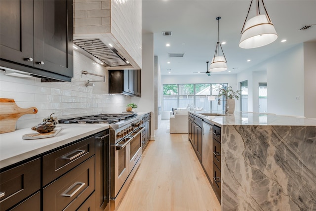 kitchen featuring range with two ovens, sink, decorative backsplash, light wood-type flooring, and decorative light fixtures