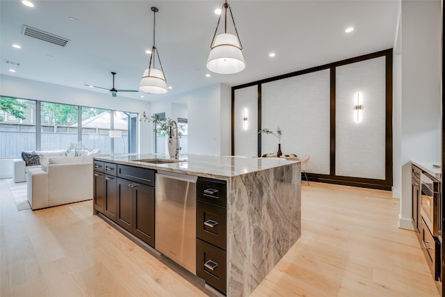 kitchen featuring pendant lighting, light wood-type flooring, stainless steel dishwasher, and an island with sink