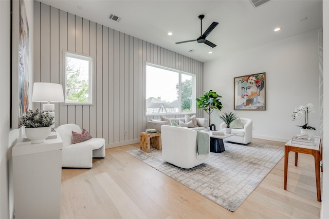 living room with light hardwood / wood-style floors, a wealth of natural light, wooden walls, and ceiling fan