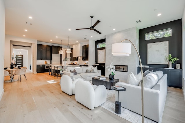 living room with a large fireplace, ceiling fan, light hardwood / wood-style floors, and a wealth of natural light