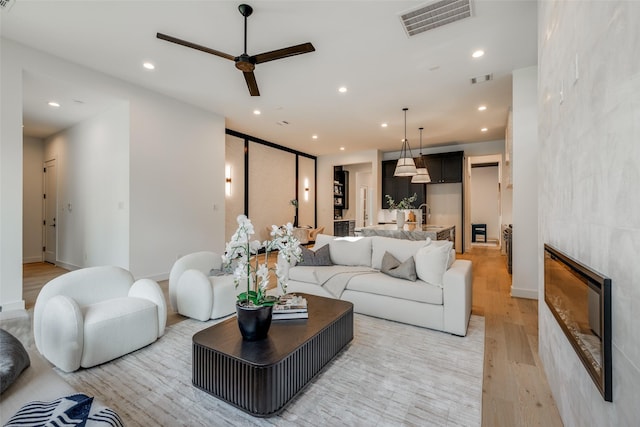 living room featuring ceiling fan, a fireplace, sink, and light wood-type flooring