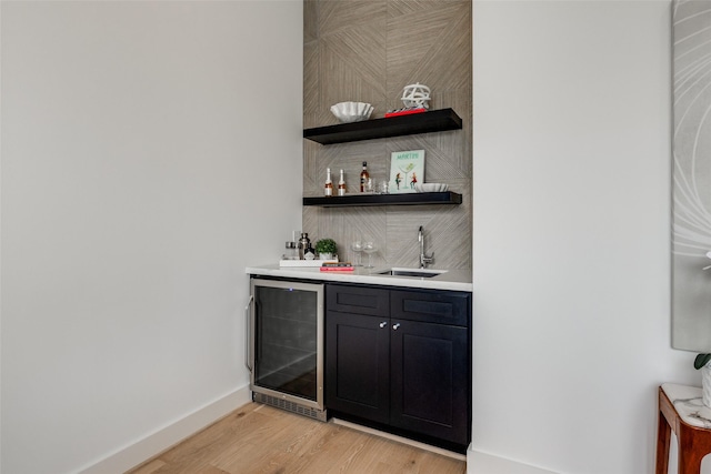 bar featuring light hardwood / wood-style floors, sink, and beverage cooler