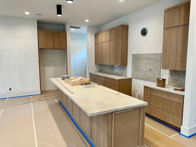 kitchen with decorative backsplash, a center island, light wood-type flooring, and light stone countertops