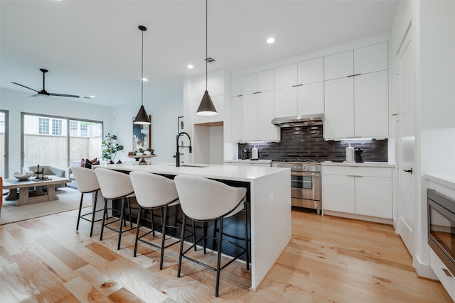 kitchen with an island with sink, light hardwood / wood-style floors, stainless steel appliances, pendant lighting, and white cabinets