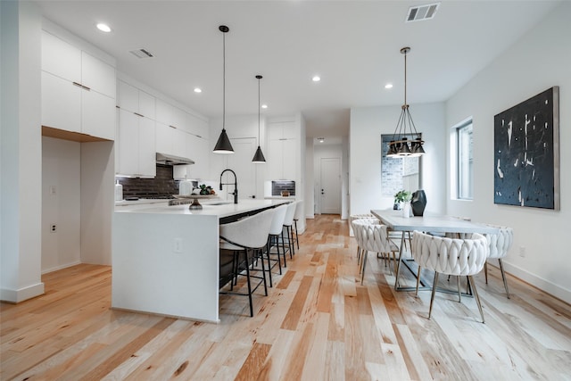 kitchen with under cabinet range hood, visible vents, backsplash, and white cabinetry