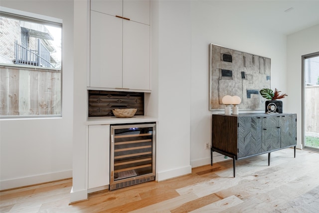 bar featuring light wood-style flooring, beverage cooler, baseboards, and a wealth of natural light