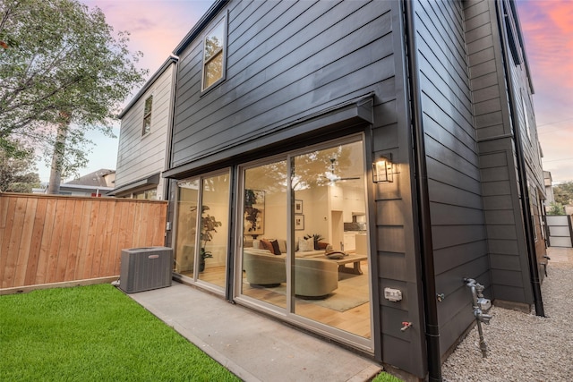 back of house at dusk featuring a yard, central AC unit, and fence