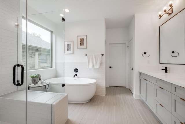 bathroom featuring a shower with shower door, a wainscoted wall, tile walls, a freestanding bath, and vanity