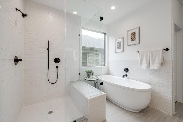 bathroom featuring a tile shower, recessed lighting, tile walls, wainscoting, and a soaking tub