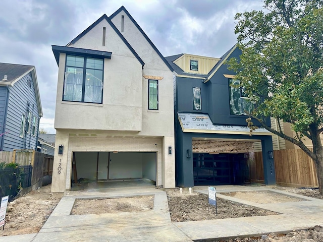 view of front of home with brick siding, stucco siding, a garage, and fence