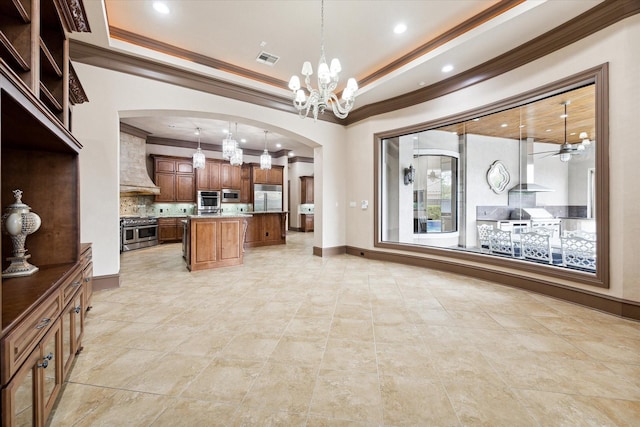 kitchen with wall chimney range hood, premium range hood, a kitchen island, pendant lighting, and built in appliances