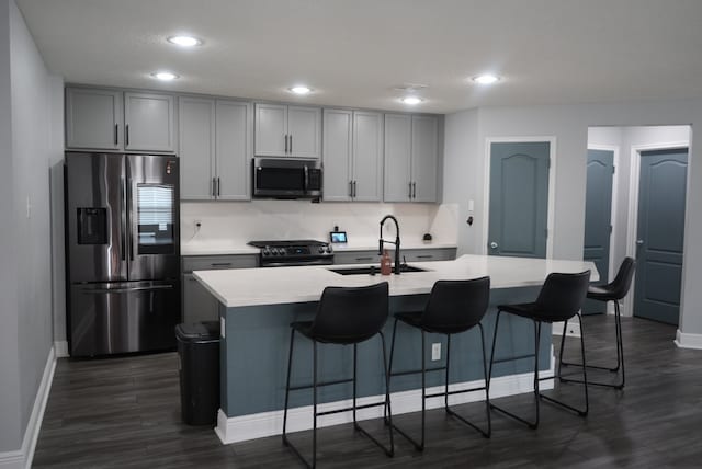 kitchen with gray cabinets, stainless steel appliances, sink, and an island with sink