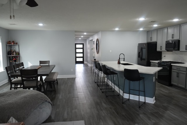 kitchen featuring dark wood-type flooring, an island with sink, sink, black appliances, and gray cabinets