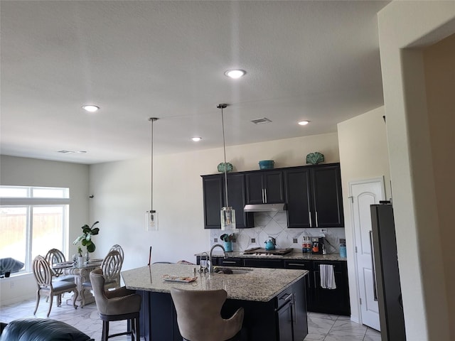 kitchen with decorative light fixtures, a kitchen bar, light stone countertops, sink, and a kitchen island with sink