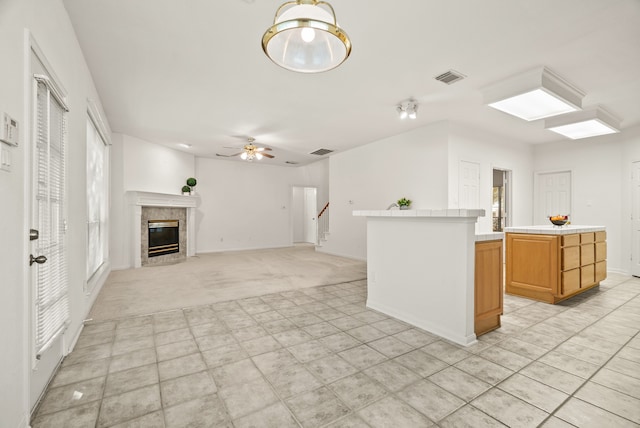 kitchen with a healthy amount of sunlight, ceiling fan, a kitchen island, a fireplace, and light colored carpet