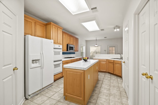 kitchen featuring kitchen peninsula, a kitchen island, tile counters, decorative light fixtures, and white appliances