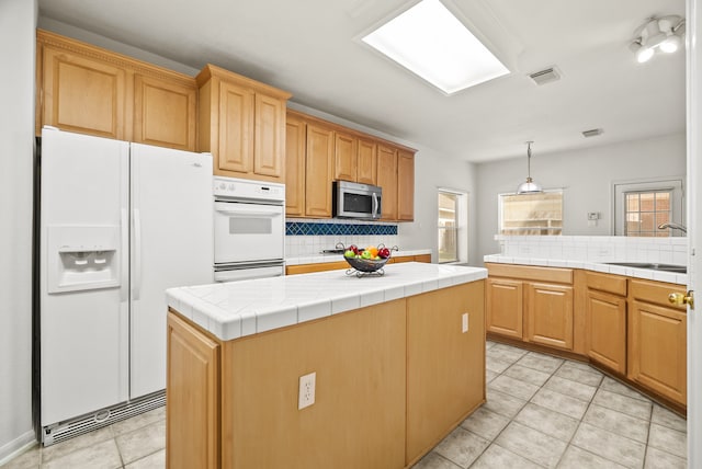 kitchen with tasteful backsplash, sink, tile counters, a center island, and white appliances