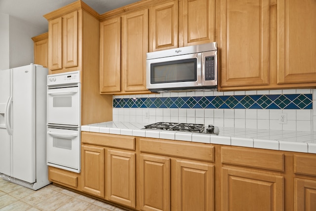 kitchen with tile countertops, stainless steel appliances, decorative backsplash, and light tile patterned floors