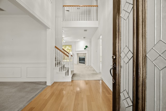 foyer with a tiled fireplace, light carpet, crown molding, and a high ceiling