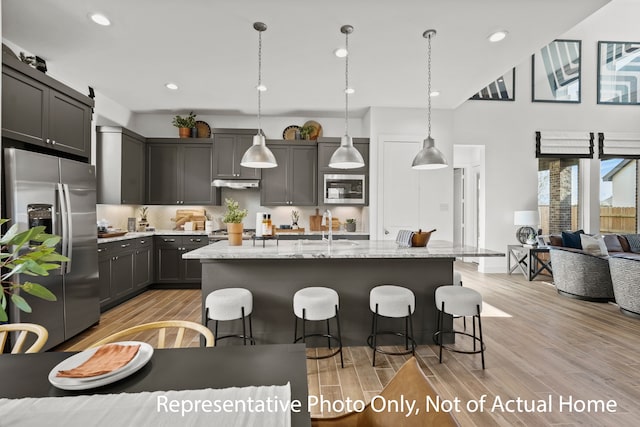 kitchen featuring light wood-type flooring, stainless steel appliances, an island with sink, and hanging light fixtures