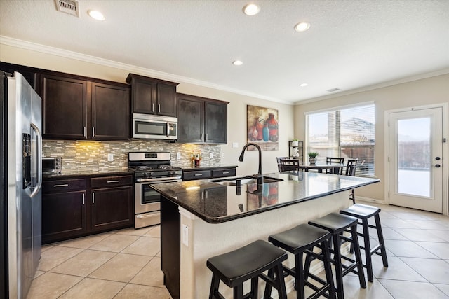 kitchen featuring a kitchen island with sink, dark stone counters, sink, a breakfast bar, and appliances with stainless steel finishes