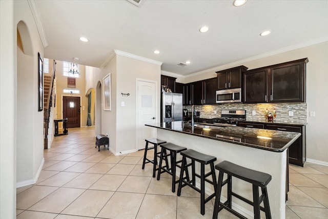 kitchen with appliances with stainless steel finishes, light tile patterned flooring, a kitchen island, dark stone countertops, and a breakfast bar area