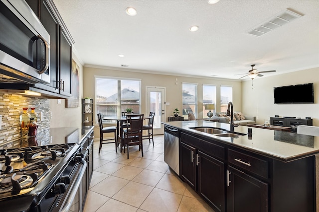 kitchen featuring an island with sink, stainless steel appliances, crown molding, sink, and light tile patterned floors