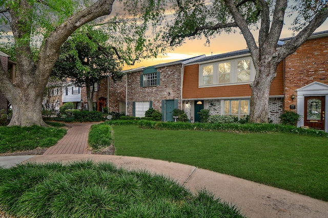 view of front of property with a garage, brick siding, and a lawn