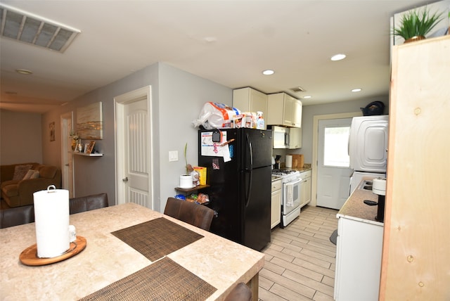 kitchen with light wood-type flooring, black fridge, white gas range, stacked washer and dryer, and white cabinets