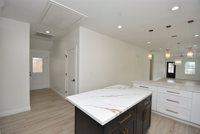 kitchen featuring a kitchen island, light stone countertops, pendant lighting, and light hardwood / wood-style floors