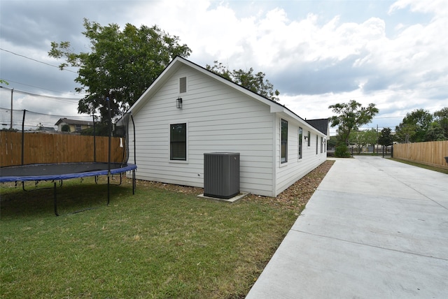 view of side of property with a patio, a trampoline, a lawn, and central AC unit