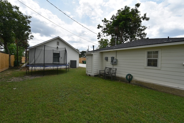 rear view of property with central AC, a lawn, and a trampoline