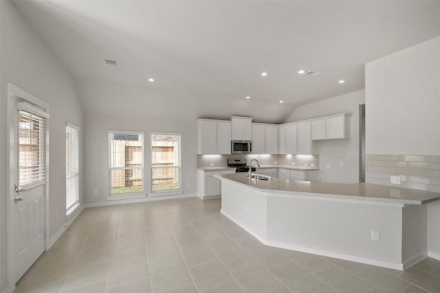 kitchen featuring lofted ceiling, stainless steel appliances, light stone countertops, light tile patterned floors, and white cabinetry