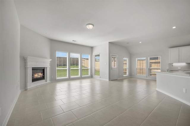 unfurnished living room with sink, light tile patterned flooring, and vaulted ceiling