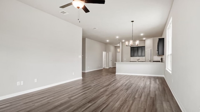 unfurnished living room featuring ceiling fan with notable chandelier and dark hardwood / wood-style flooring