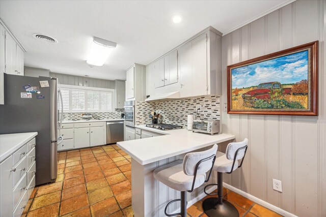 kitchen with stainless steel appliances, white cabinetry, kitchen peninsula, a breakfast bar area, and backsplash