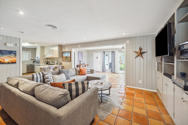 living room featuring light tile patterned flooring, wooden walls, and ornamental molding