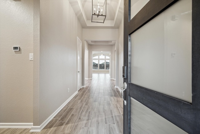 hallway featuring a notable chandelier, a tray ceiling, and light wood-type flooring