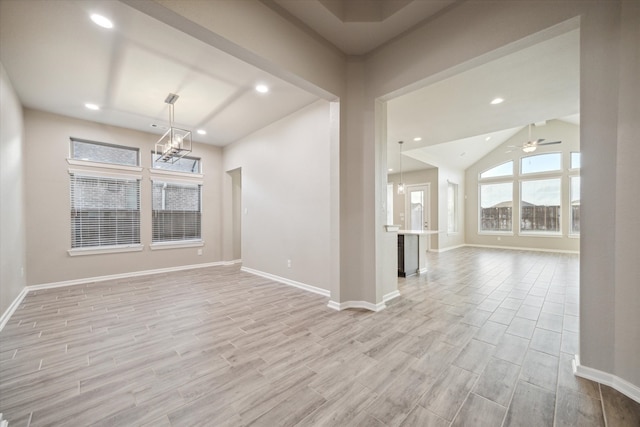 empty room featuring vaulted ceiling, light wood-type flooring, and ceiling fan with notable chandelier