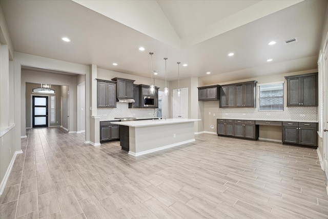 kitchen featuring dark brown cabinetry, a kitchen island with sink, hanging light fixtures, and light hardwood / wood-style flooring