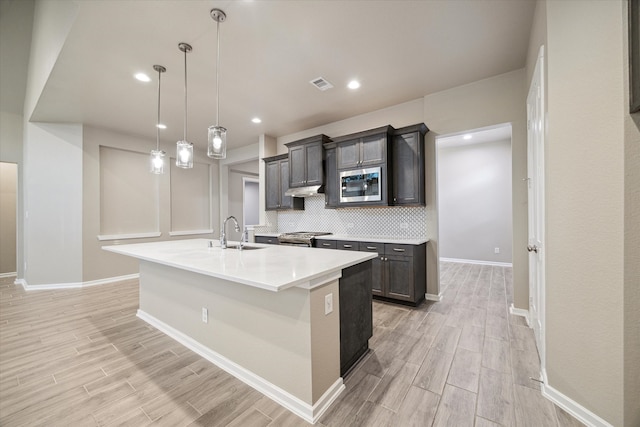 kitchen featuring sink, stainless steel appliances, decorative light fixtures, decorative backsplash, and a kitchen island with sink