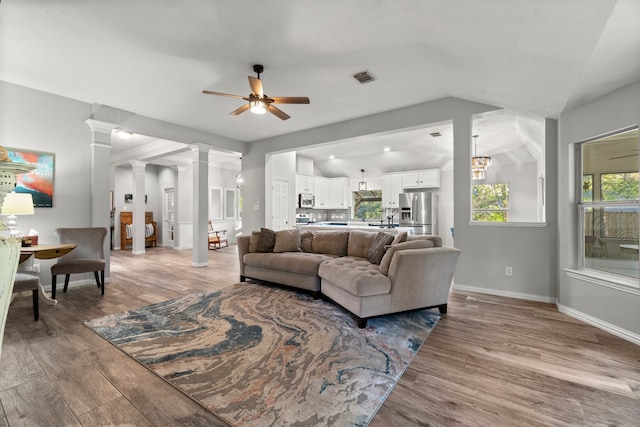 living room featuring lofted ceiling, wood-type flooring, ornate columns, and ceiling fan with notable chandelier