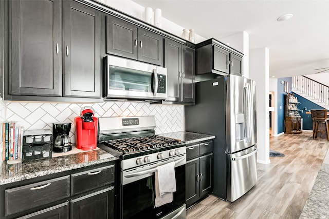 kitchen featuring tasteful backsplash, ceiling fan, light hardwood / wood-style flooring, dark stone countertops, and stainless steel appliances