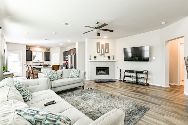 living room with light hardwood / wood-style flooring, a tiled fireplace, and ceiling fan