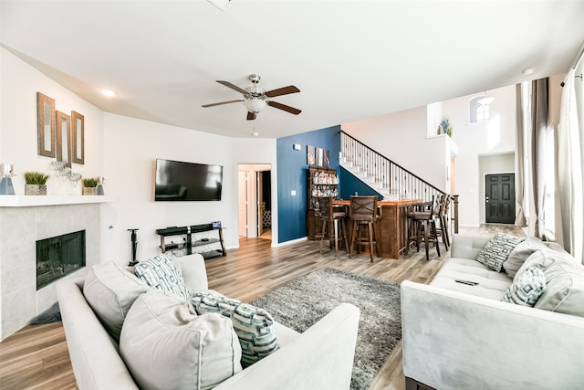 living room featuring light hardwood / wood-style flooring, indoor bar, a tile fireplace, and ceiling fan