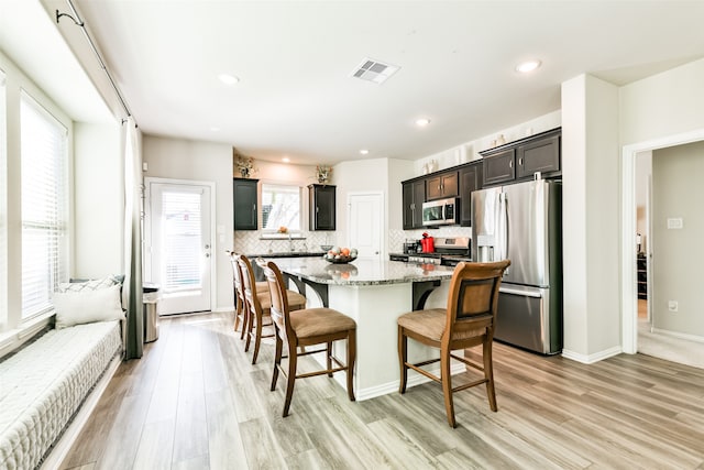 kitchen with a kitchen island, appliances with stainless steel finishes, a breakfast bar, light stone countertops, and light wood-type flooring