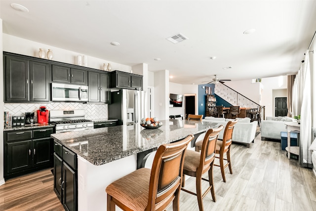 kitchen featuring a breakfast bar, a center island, stainless steel appliances, dark stone countertops, and light hardwood / wood-style flooring