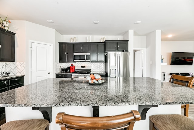 kitchen with a spacious island, stainless steel appliances, stone counters, and a breakfast bar area