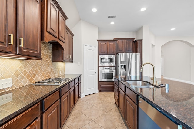 kitchen featuring decorative backsplash, light tile patterned floors, appliances with stainless steel finishes, dark stone countertops, and sink